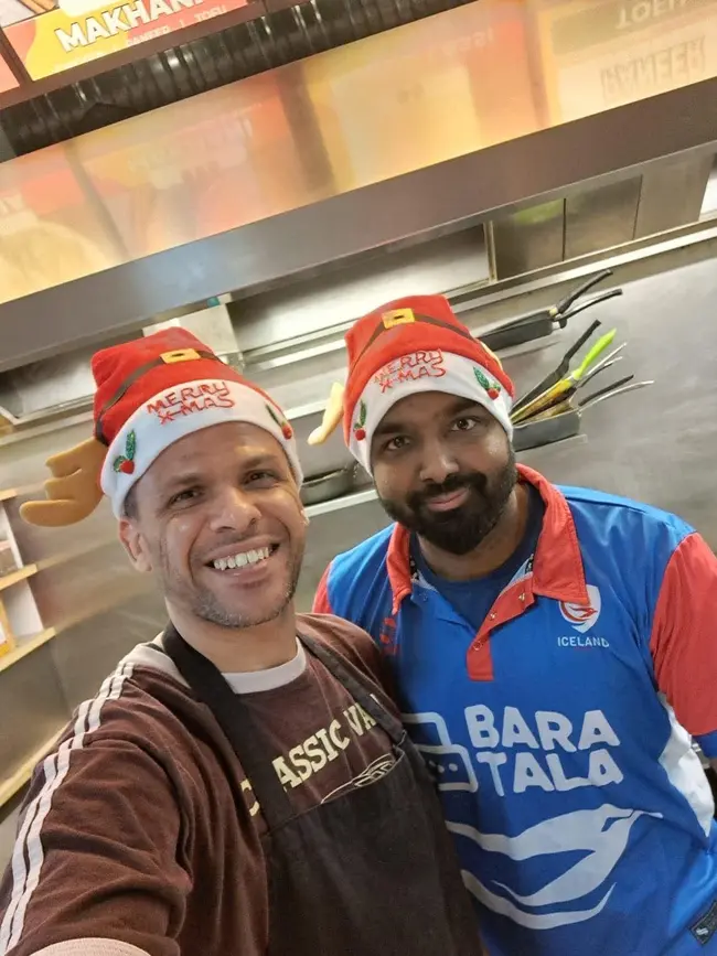 Two friends smiling together in the kitchen, wearing festive hats