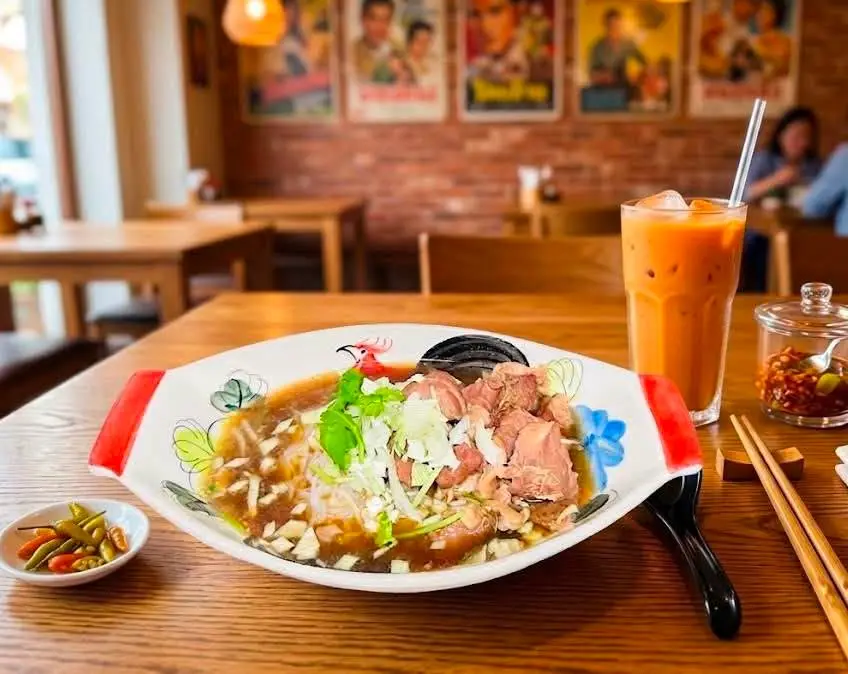 Noodle soup and Thai iced tea on a table inside Aroy Dee, with the restaurant dining area behind